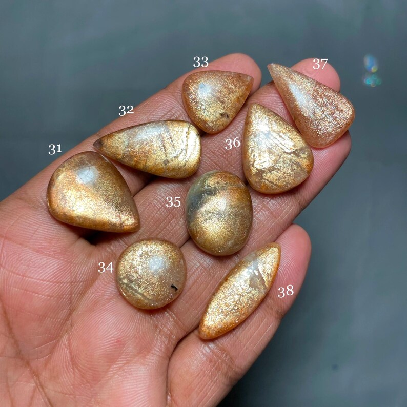 May include: Eight gold sunstone cabochons, each with a unique pattern of shimmering inclusions. The stones are numbered 31 through 38.
