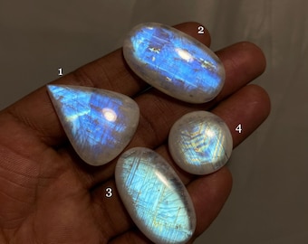 May include: Four iridescent moonstone cabochons in various shapes and sizes. The stones are white with blue and green iridescent flashes.