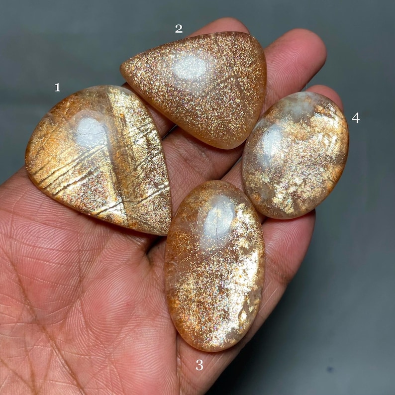 May include: Four sunstone cabochons in various shapes and sizes, with a golden brown color and a shimmery, iridescent finish.