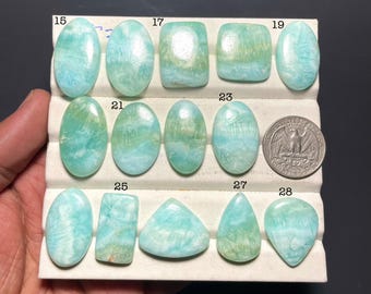 Peut inclure: Une collection de pierres précieuses polies de formes variées, dont des ovales, des rectangles et des gouttes. Les pierres présentent des teintes bleu clair et vertes, avec une pièce de monnaie pour l'échelle. Les pierres sont disposées sur un présentoir blanc.