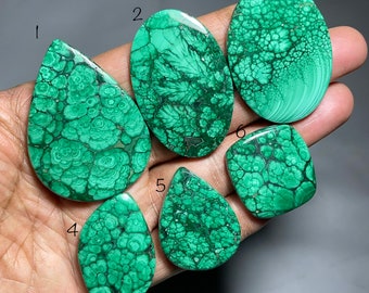 Puede incluir: Una colección de seis piedras preciosas de malaquita pulidas en varias formas, incluyendo ovaladas, en forma de lágrima y rectangulares. Las piedras muestran un color verde vibrante con patrones y texturas intrincados. Las piedras preciosas se sostienen en una mano.