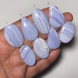 Puede incluir: Ocho cabujones de ágata azul con bandas blancas, numerados del 1 al 8, dispuestos en fila sobre una mano.