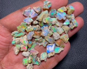 May include: A collection of small, rough, iridescent opal gemstones in various shades of green, blue, and white. The opals are in a hand, and some have a rough, natural texture.
