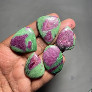 May include: Five green and pink gemstone cabochons, numbered 1 through 5, are displayed on a hand. The cabochons are various shapes and sizes.