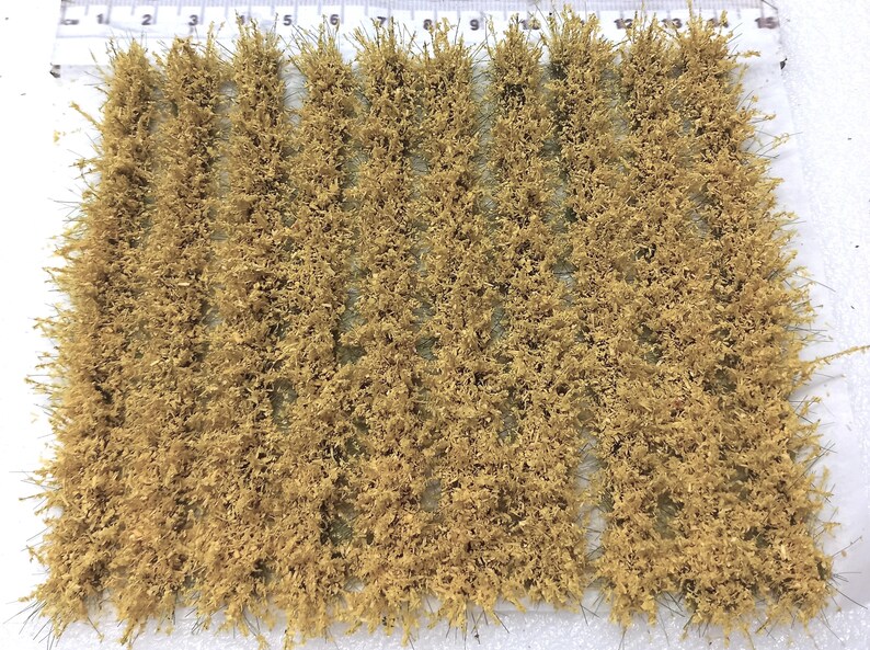 May include: A sheet of light brown, dry, static grass tufts, arranged in rows. The grass is approximately 1 inch in length.