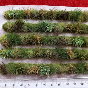 May include: Eight strips of green, brown, and white artificial grass for model railroading or miniature landscaping. Each strip is approximately 14 inches long.