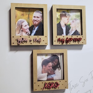 May include: Three wooden picture frames with couples in photos. The frames have a light brown wood finish and are decorated with small gold hearts. The text on the frames reads "you + me", "my forever", and "xoxo".