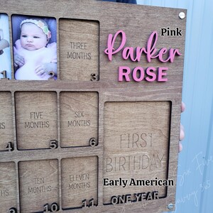 May include: Wooden baby milestone photo frame with spaces for photos and months. Features the name "Parker Rose" in pink, with text for "First Birthday" and "Early American". Includes spaces for photos from 1 to 11 months.