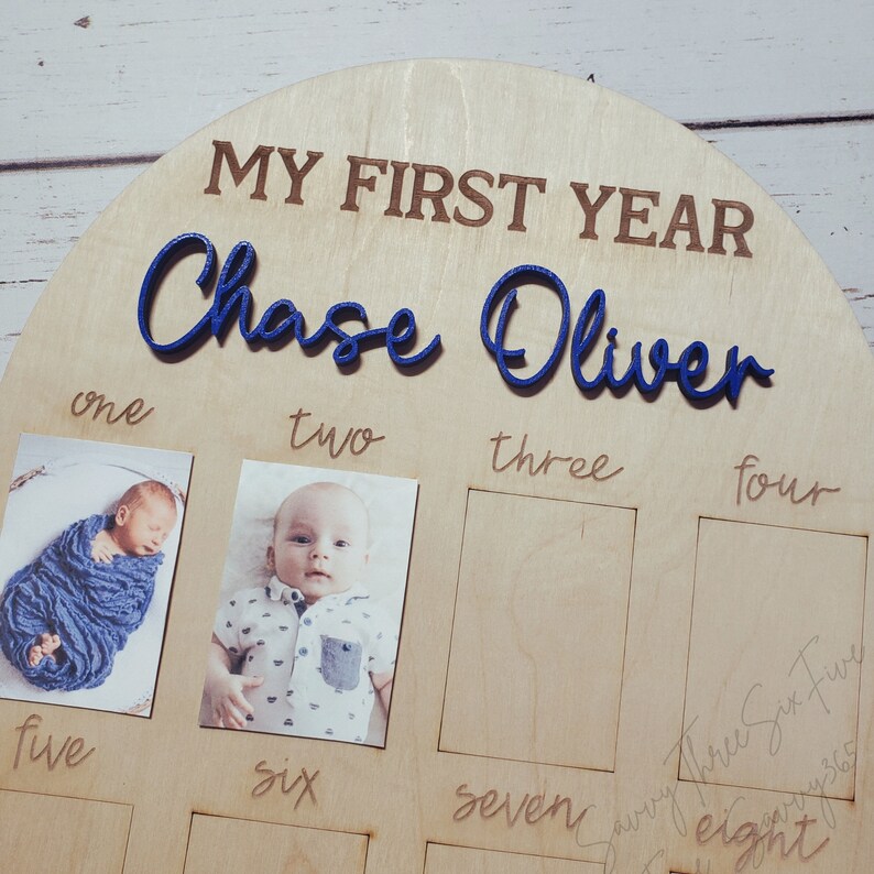 May include: A wooden photo frame with the words "My First Year" and the name "Chase Oliver" in blue lettering. The frame has eight slots for photos, with the first two slots filled with photos of a baby boy.