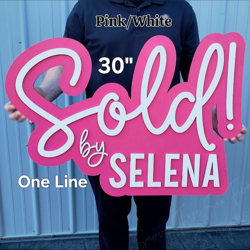 May include: A large, pink wooden sign with the word "Sold" in white script, measuring 30 inches. The sign also includes the text "by SELENA" in white. The sign is designed with a cursive font.