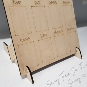 May include: Wooden number learning board with slots for numbers one through twelve. The board is made of light brown wood and has a stand. The numbers are written in cursive.