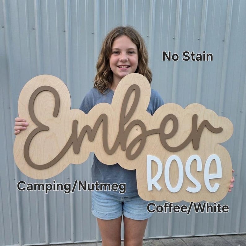 May include: A custom wooden sign featuring the name Ember Rose in layered lettering. The word Ember is in a brown script font, and the word Rose is in a white block font. The sign has a light wood backing with the text No Stain, Camping/Nutmeg, and Coffee/White.