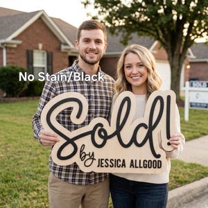 May include: A wooden sign with the word "Sold!" in black script, held by two people. The sign also includes the text "by JESSICA ALLGOOD" in a smaller font. The sign has a natural wood finish and the text "No Stain/Black" is in the upper left corner.