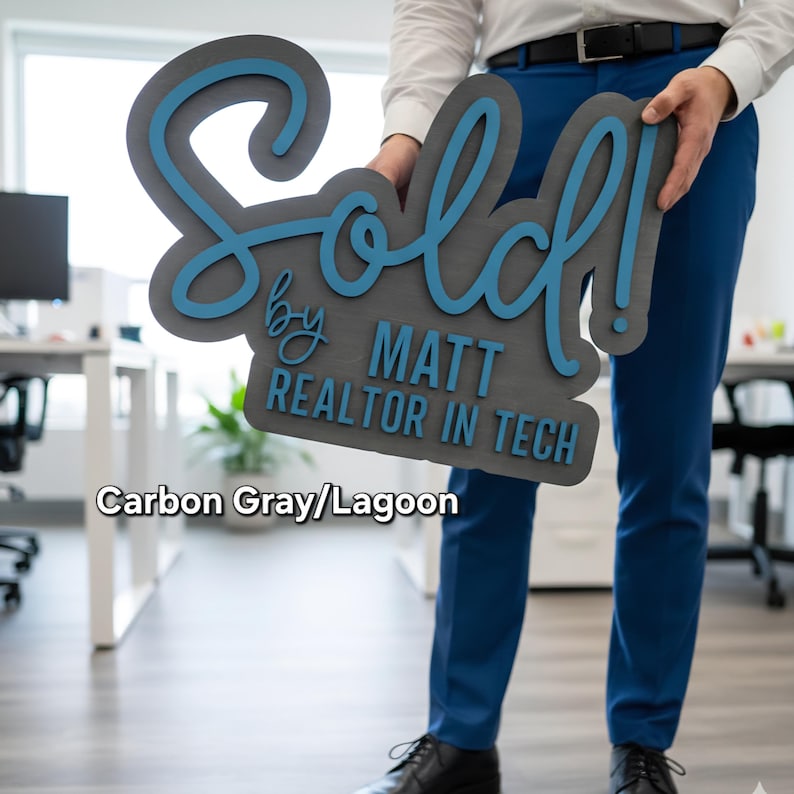 May include: A carbon gray sign with the word "Sold!" in a script font, accented with lagoon blue. The sign also includes the text "by MATT REALTOR IN TECH".