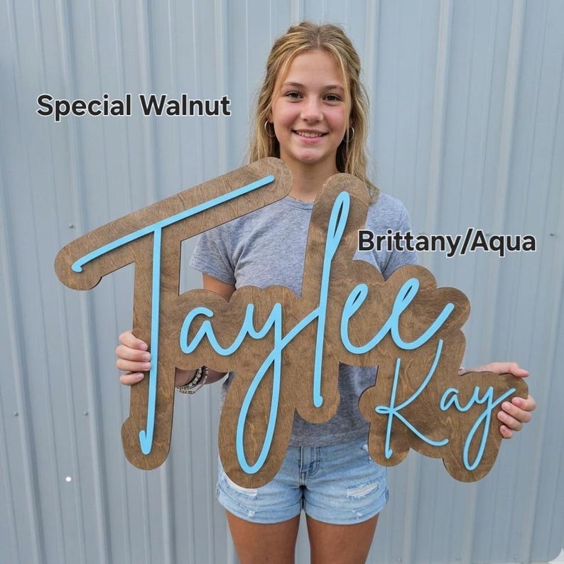 May include: A custom wooden name sign featuring the name Taylee Kay in a script font. The base is a dark brown Special Walnut wood finish, and the raised lettering is in a bright aqua colour. The text Special Walnut and Brittany/Aqua is visible.