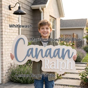 May include: A custom wooden name sign featuring the name Canaan in slate blue script lettering layered over a light wood backing, with the name Ralph in white block lettering below. The sign includes text labels for Whitewash, Marshmallow/Slate Blue, and Lemon Sage/White.