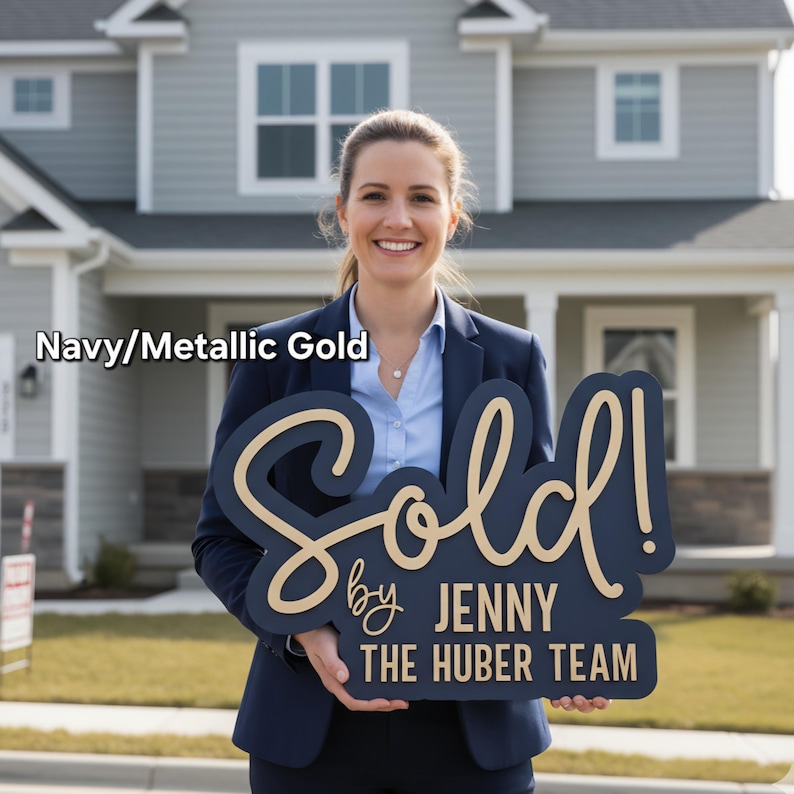 May include: Navy and metallic gold "Sold" sign held in front of a house. The sign reads "Sold by Jenny The Huber Team" in a stylish font. The sign is a navy blue color with metallic gold lettering.