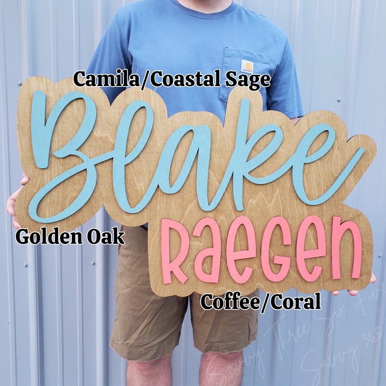 May include: A wooden sign with a golden oak finish featuring the name Blake in light blue script and the name RAEGEN in coral block letters. Text overlays include Camila/Coastal Sage, Golden Oak, and Coffee/Coral identifying the colours.