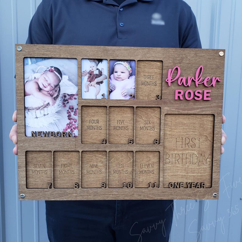May include: Wooden baby milestone photo frame with spaces for photos from newborn to one year. The frame includes the name "Parker Rose" in pink letters. The frame has spaces for photos labeled "Newborn", "Three Months", "Four Months", "Five Months", "Six Months", "Seven Months", "Eight Months", "Nine Months", "Ten Months", "Eleven Months", and "First Birthday".