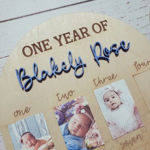 May include: A wooden photo frame with the words "One Year Of Blakely Rose" engraved on it. The frame has four slots for photos, labeled "one", "two", "three", and "four".
