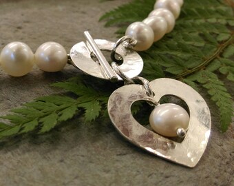 Handmade natural white freshwater pearl bracelet with hammered silver toggle fastening and silver heart charm. Bridal. Wedding jewellery.