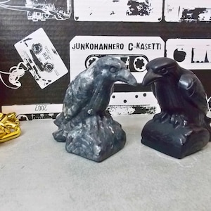 Puede incluir: Dos pequeñas figuritas de cuervo detalladas. Una es negra y la otra es gris. Ambas están posadas sobre una base y tienen una apariencia realista.