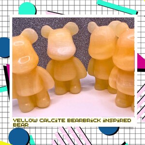 May include: Four yellow calcite Bearbrick-inspired bear figurines. The figures are standing on a white surface. The text "YELLOW CALCITE BEARBRICK INSPIRED BEAR" is at the bottom of the image.