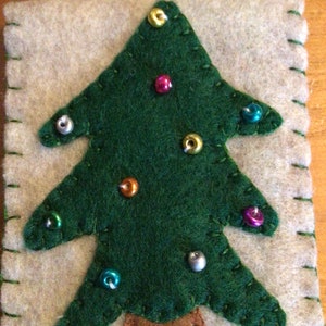 May include: A felt Christmas tree ornament with a brown felt trunk and green felt leaves. The tree is decorated with colorful beads.