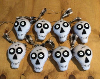 Puede incluir: Ocho adornos de calavera de fieltro blanco con ojos de botón negro, narices triangulares negras cosidas y líneas de boca. Cada calavera tiene un lazo de tela a cuadros blanco y negro y un cordel fino de color marrón para colgar.