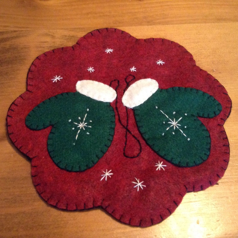 K&ouml;nnte beinhalten: Ein roter Filz-Anh&auml;nger mit zwei gr&uuml;nen Filz-Handschuhen mit wei&szlig;en Manschetten und Schneeflocken-Stickerei. Der Anh&auml;nger ist mit wei&szlig;en Schneeflocken-Stickereien verziert.