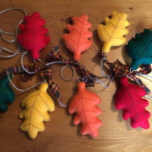 May include: A garland of felt leaves in shades of red, orange, yellow, and green. The leaves are sewn together with twine and ribbon, and are strung on a length of twine.