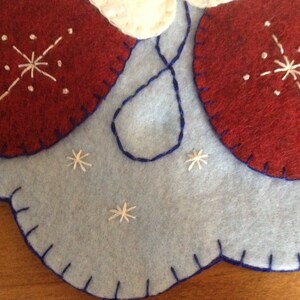 K&ouml;nnte beinhalten: Ein blauer Filz-Weihnachtsbaumschmuck mit roten Filz-Anh&auml;ngern und wei&szlig;en gestickten Schneeflocken.