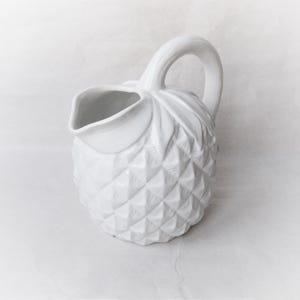 Peut inclure: Pichet en céramique blanche en forme d'ananas avec une surface texturée. Le pichet a une poignée et un bec.