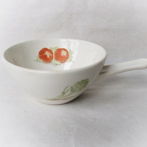 May include: White ceramic soup bowl with a handle. The bowl features a simple design with two red tomatoes and green leaves painted on the inside.