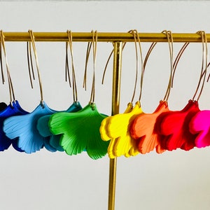 Peut inclure: Une présentation de 10 paires de boucles d'oreilles en forme de feuille de ginkgo dans un arc-en-ciel de couleurs, suspendues à un support doré. Les boucles d'oreilles sont en argile polymère et ont un aspect texturé et réaliste.