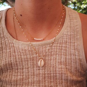 Peut inclure: Un collier en or à plusieurs rangs avec un petit pendentif en forme de coquillage blanc. Le collier est composé de chaînes délicates et de petites perles blanches.