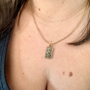 Peut inclure: Un collier en chaîne dorée avec un petit pendentif rectangulaire. Le pendentif a un design détaillé.