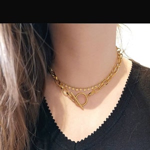 Puede incluir: Un collar de oro de dos capas con cierre de palanca. El collar presenta una cadena gruesa con eslabones ovalados y una cadena m&aacute;s fina con peque&ntilde;as cuentas redondas.