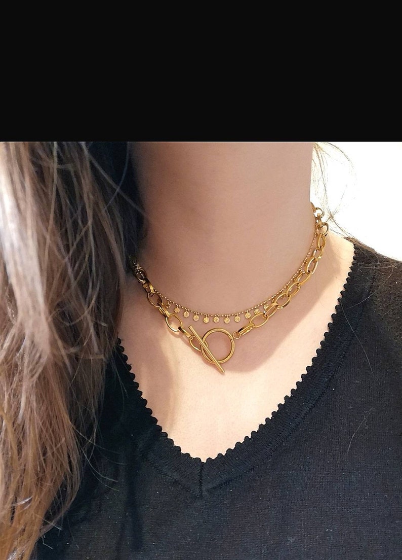 Puede incluir: Un collar de oro de dos capas con cierre de palanca. El collar presenta una cadena gruesa con eslabones ovalados y una cadena m&aacute;s fina con peque&ntilde;as cuentas redondas.