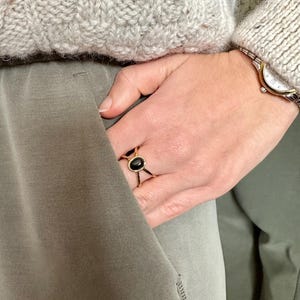 May include: A gold ring with a black oval gemstone. The ring is worn on the index finger of a hand with a watch on the wrist.