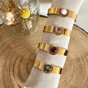 May include: Four gold bracelets with different colored gemstones. Each bracelet has a sunburst design around the gemstone.