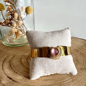 May include: A gold bangle bracelet with a pink stone set in a sunburst design.
