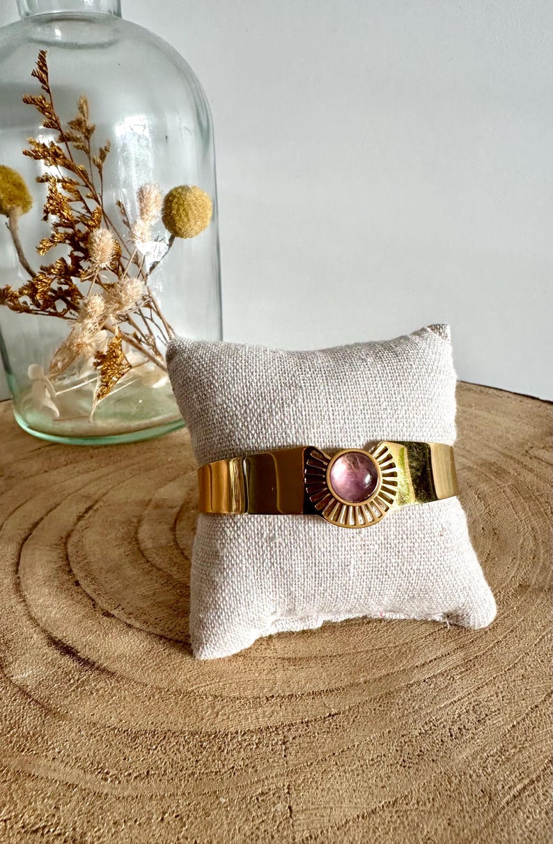 May include: A gold bangle bracelet with a pink stone set in a sunburst design.