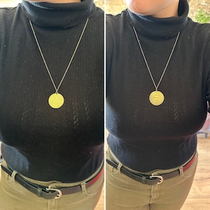 Peut inclure: Un collier en or avec un pendentif rond orné d'un motif soleil. Le collier est porté par une personne vêtue d'un pull noir à col roulé et d'un pantalon kaki.