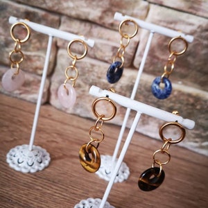 Op de afbeelding: Vier paar gouden creolen met een hangende ketting en een edelsteenbedel. De bedels zijn roze, blauw en bruin.