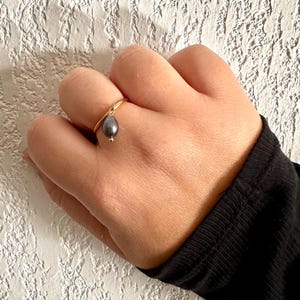 May include: A gold ring with a dangling black pearl.
