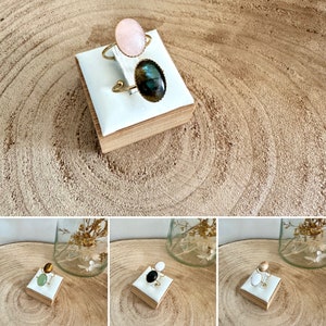 May include: Three oval-shaped gemstone rings on small wooden display stands. The rings are gold-toned and feature a pink, green, and black gemstone.