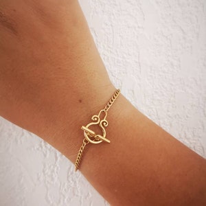 Può includere: Un braccialetto a catena dorata con una chiusura a levetta unica. La chiusura è un design decorativo con una piccola barra che scorre attraverso un anello.