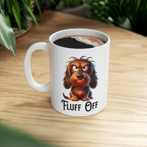 May include: White ceramic coffee mug with a cartoon image of a brown and black dog with a grumpy expression. The text "Fluff Off" is printed below the dog.