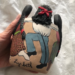 May include: Hand-painted ceramic planter with a folk art design featuring three figures dancing. The figures are painted in shades of red, green, blue, and brown. The planter is signed "Lisa Beth".